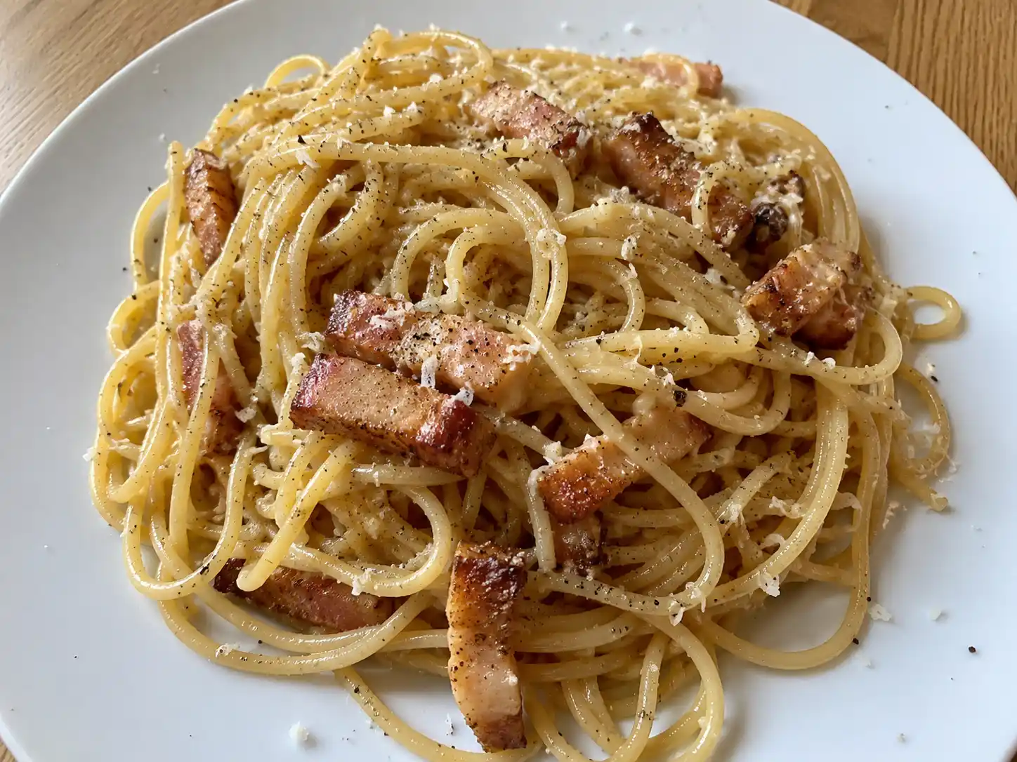äkta carbonara på vit tallrik med spaghetti, guanciale, pecorino och svartpeppar i varmt sidoljus från köksfönster