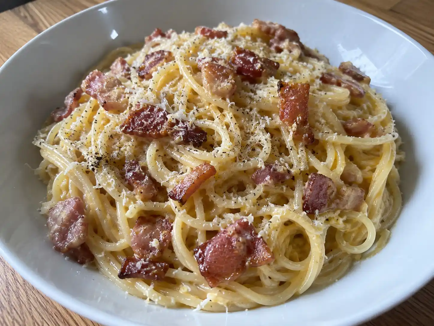 carbonara med bacon serverad i djup tallrik med blank sås, knaprigt bacon, parmesan och grovmalen svartpeppar.