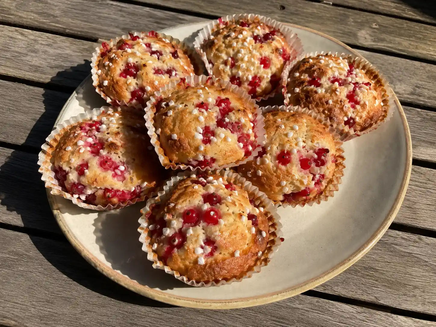 muffins med röda vinbär med gyllene topp, röda bär och pärlsocker på ett enkelt fat